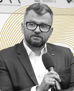 Mężczyzna w okularach i garniturze trzymający mikrofon podczas prezentacji